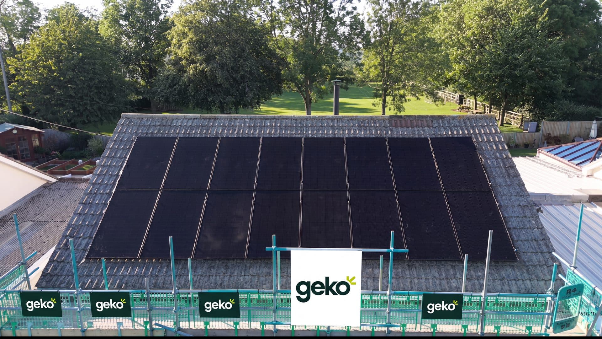 Sixteen black solar panels on a tiled roof in Somerset, fitted by Geko Energy, with Geko-branded scaffolding in front